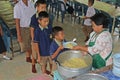 Students stand in row and receive food from the woman cook.